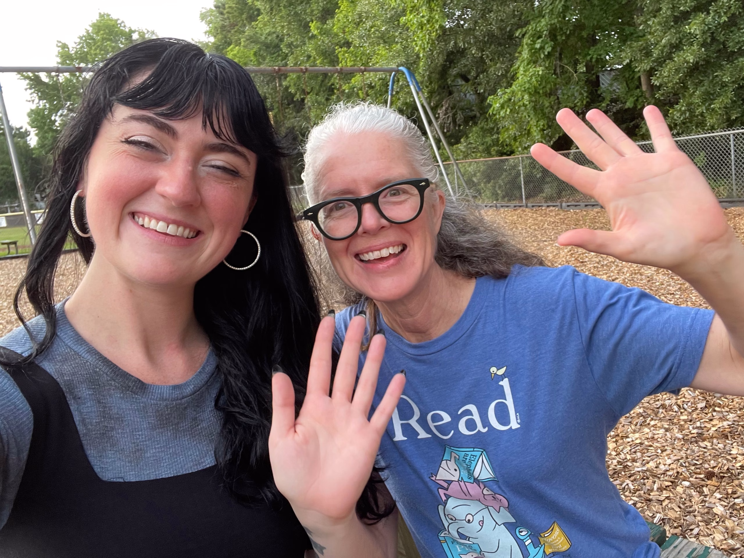 Coco and Sharon smile and wave. Sharon has grey hair and glasses and is wearing an Elephant and Piggy T-shirt. Coco has black hair with bangs and cute hoop earings.